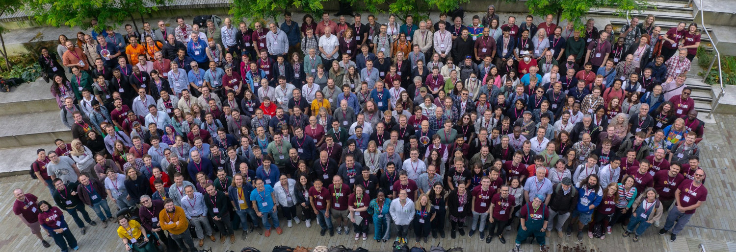 The attendees at RSECon24 - about 400 people clustered together, smiling up at the camera.