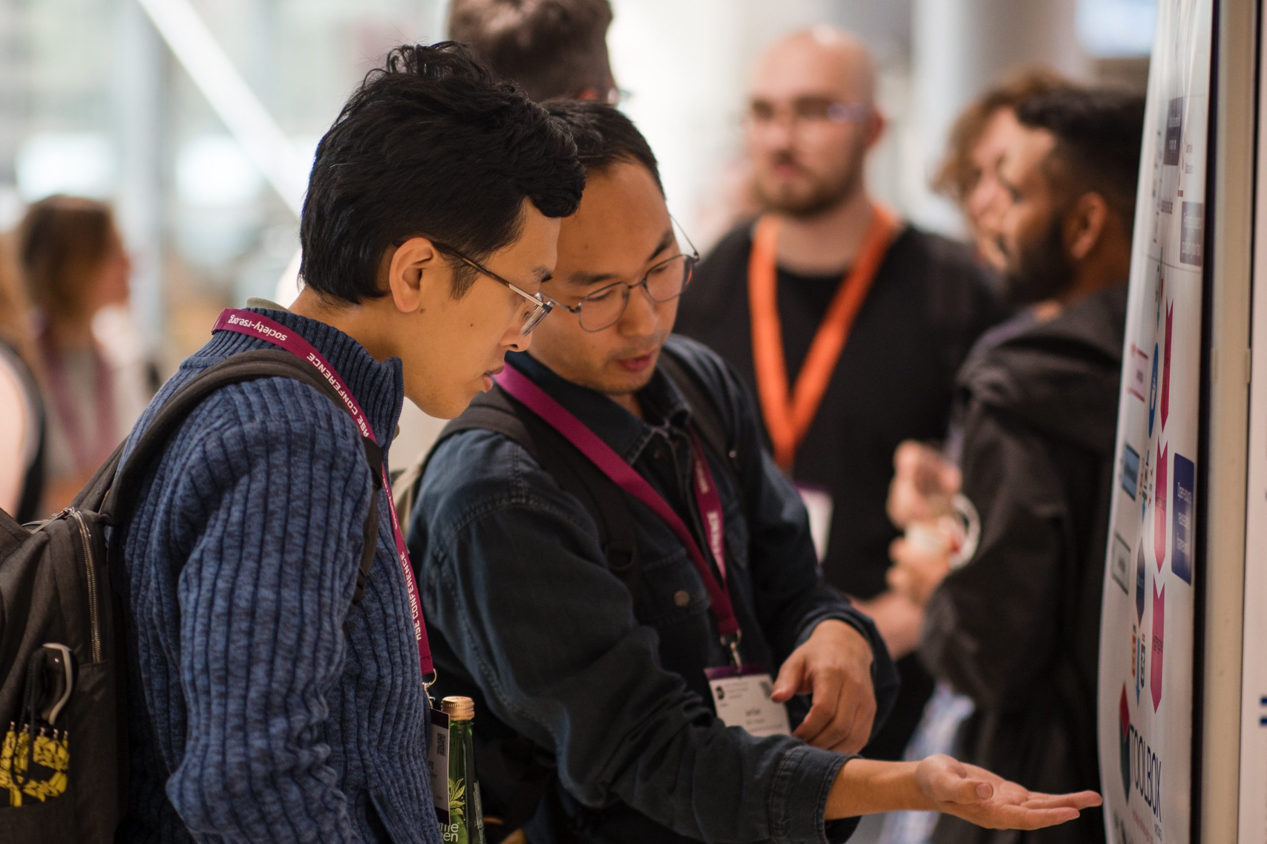Two people wearing conference lanyards look at a poster together.